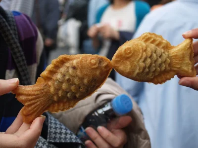 To personer holder taiyaki kager op, så det ligner fiskene kysser