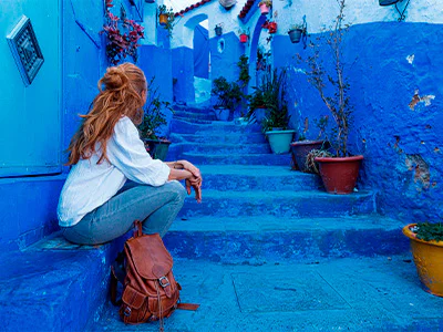 Kvinde sidder ved trappe i den blå by, Chefchaouen, i Marokko